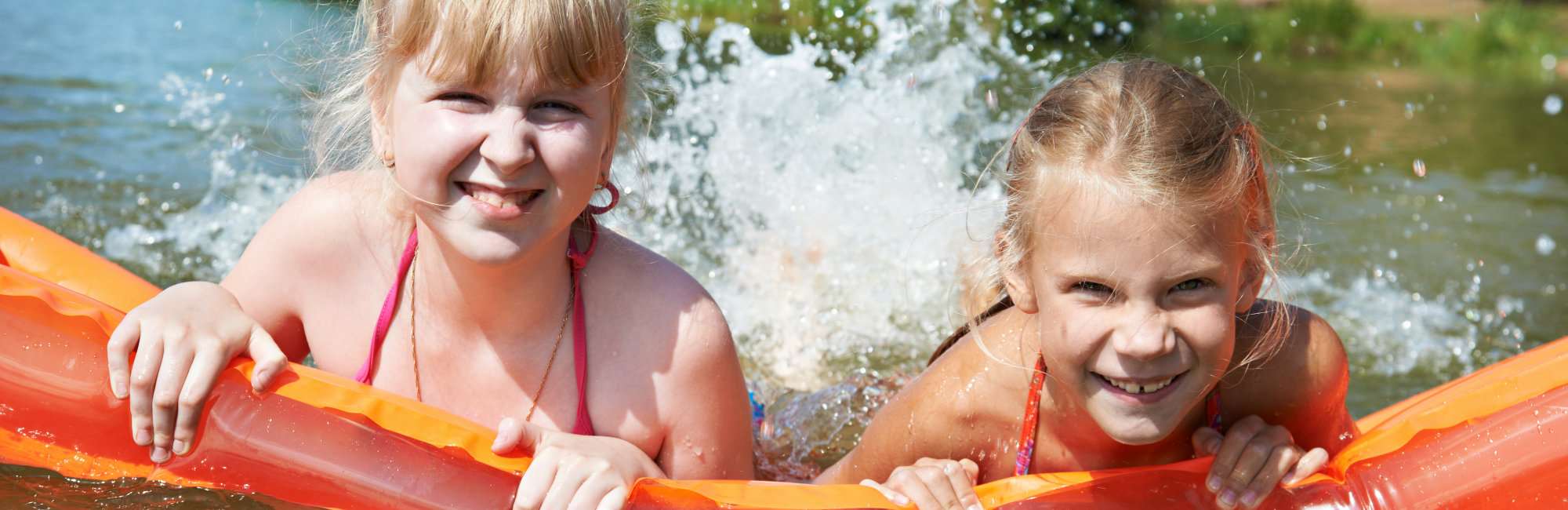 Happy little girls on mattress in lake at summer