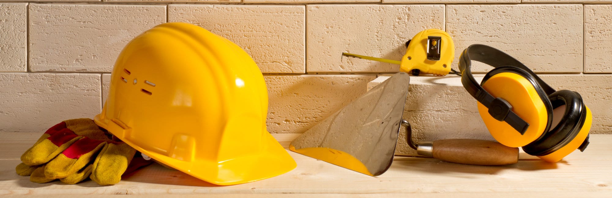 beige brick background, yellow helmet and trowel on a wooden floor